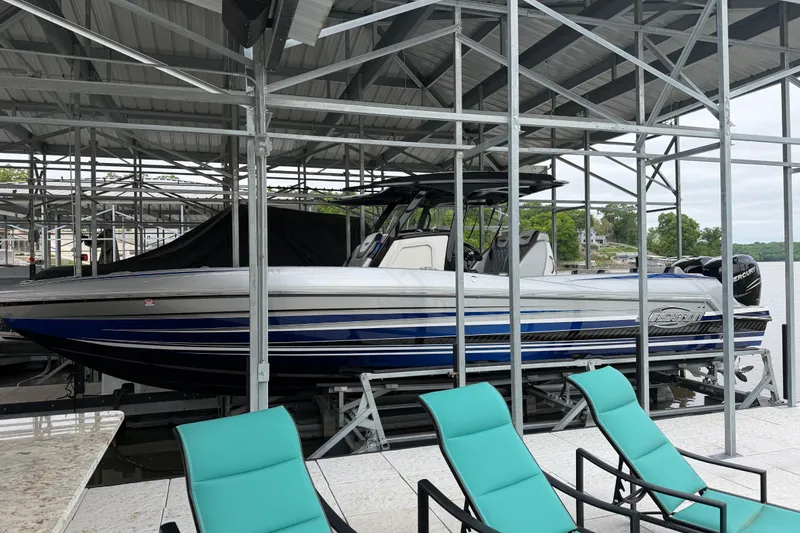 The Image of 2018 Sunsation 32 CCX boat docked under a metal canopy, with turquoise chairs nearby. - 1