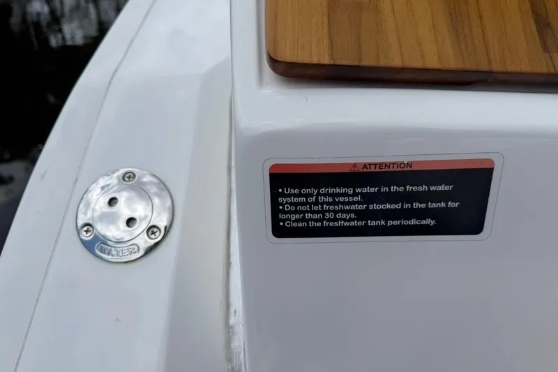Slide: The Image of 2025 NX Boats 340 Sport Coupe freshwater system warning label and water inlet. - 29