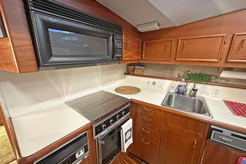 Slide: The Image of 1988 Ocean Yachts 48 Super Sport kitchen with microwave, stove, sink, and wooden cabinetry. - 21