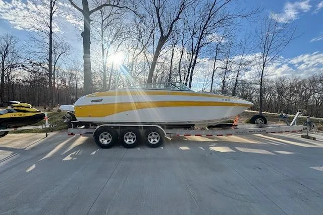 Slide: The Image of 2003 Crownline 270 BR boat on trailer, parked outdoors with sunlit trees in background. - 2