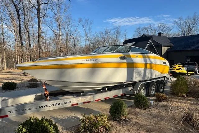 Slide: The Image of 2003 Crownline 270 BR boat on trailer, parked outdoors, surrounded by trees and shrubs. - 4