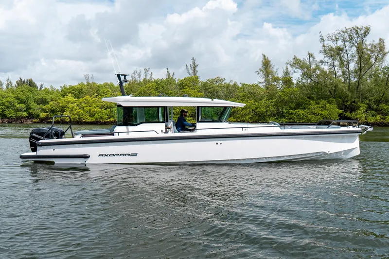 The Image of 2022 Axopar 37 XC Cross Cabin boat cruising on a calm river with lush greenery. - 0