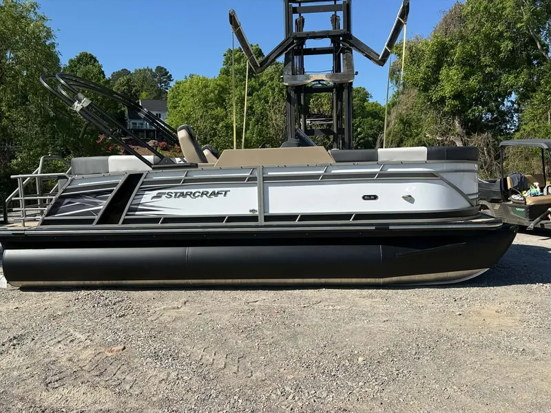 Slide: The Image of 2026 Starcraft SLS-1 R pontoon boat on gravel surface, surrounded by trees. - 28