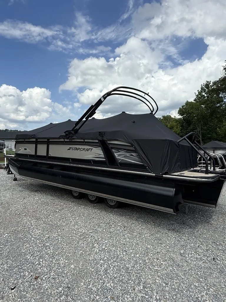 Slide: The Image of 2025 Starcraft SLS-3 pontoon boat with cover on gravel surface. - 4