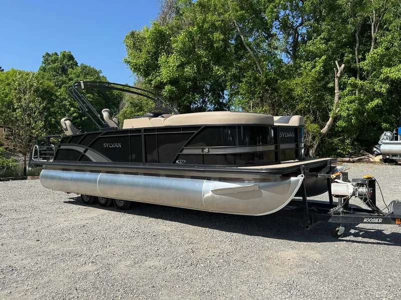 Slide: The Image of 2025 Sylvan L-3 Party Fish pontoon boat on trailer, surrounded by trees. - 24