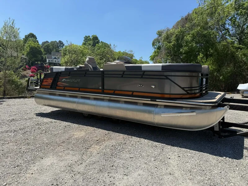 The Image of 2025 Starcraft SLS-3 pontoon boat on gravel lot, surrounded by trees. - 1