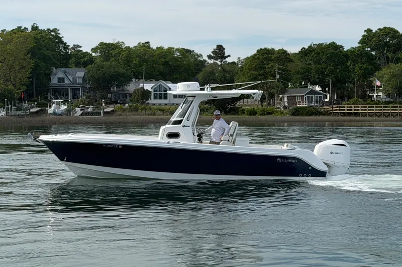 Slide: The Image of 2021 Edgewater 262CC boat cruising on a calm lake near waterfront homes. - 12