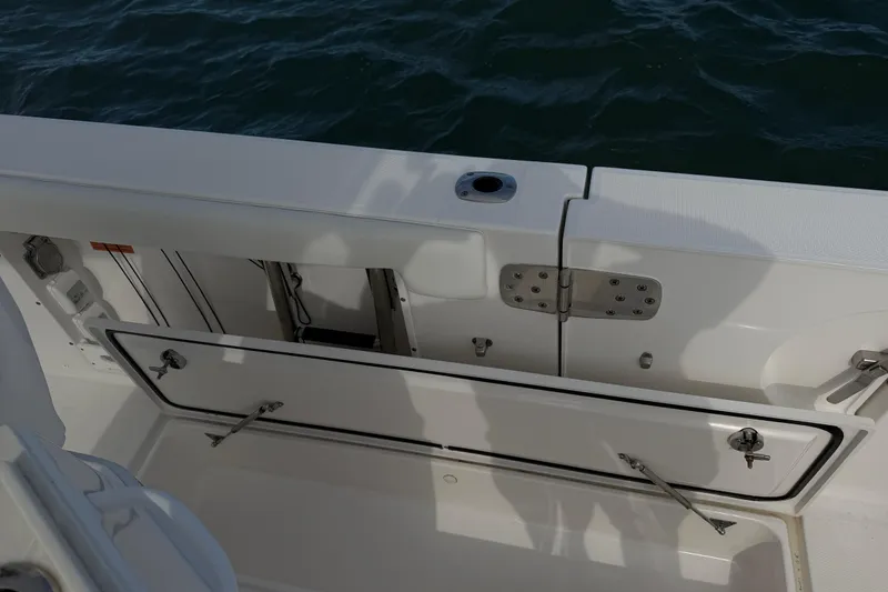 Slide: The Image of 2021 Edgewater 262CC boat interior with open storage compartment, near water. - 56