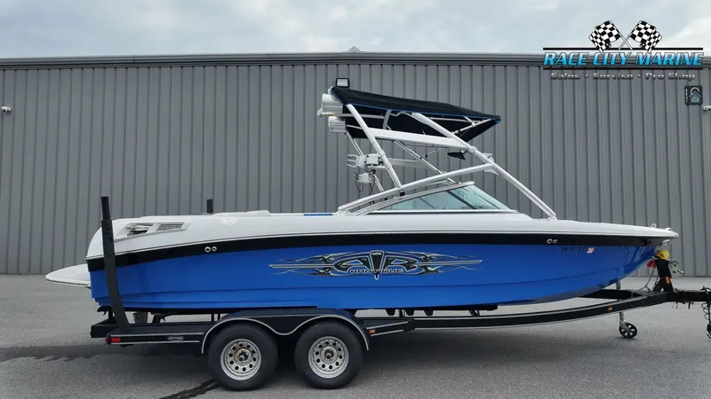 The Image of 2007 Correct Craft 236TE boat on trailer in front of gray building. - 1