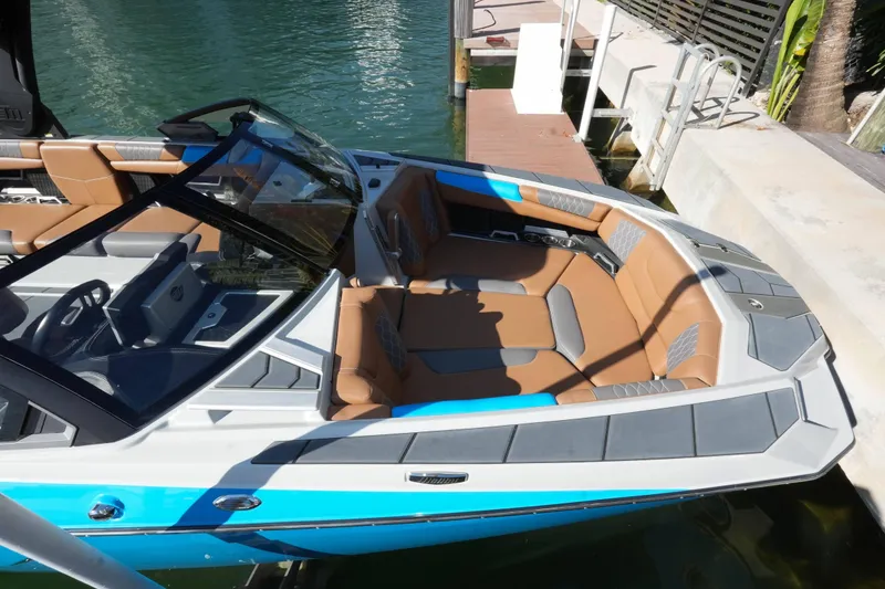 Slide: The Image of 2020 Malibu M240 boat with tan and gray seating, docked by the water. - 23