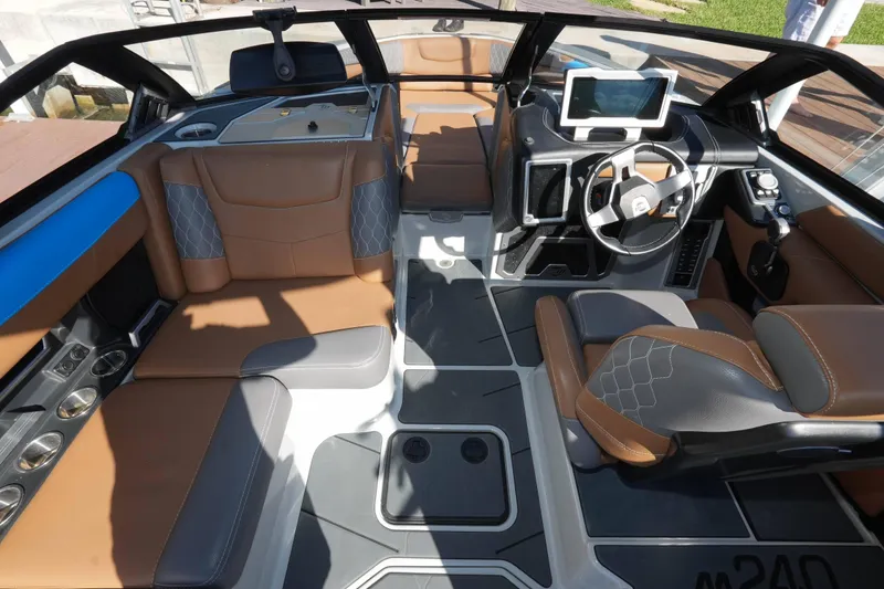 Slide: The Image of 2020 Malibu M240 boat interior with brown and gray seating, modern dashboard, and steering wheel. - 28