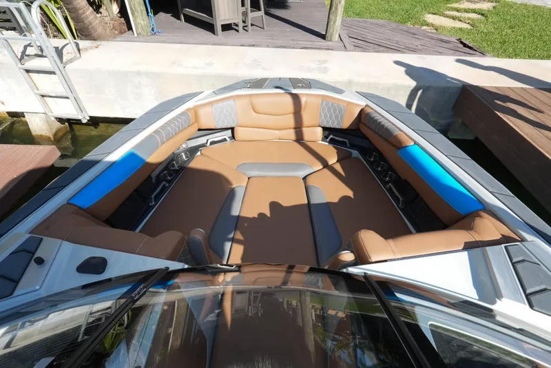 Slide: The Image of 2020 Malibu M240 boat interior with brown and blue seating, docked by a wooden deck. - 29