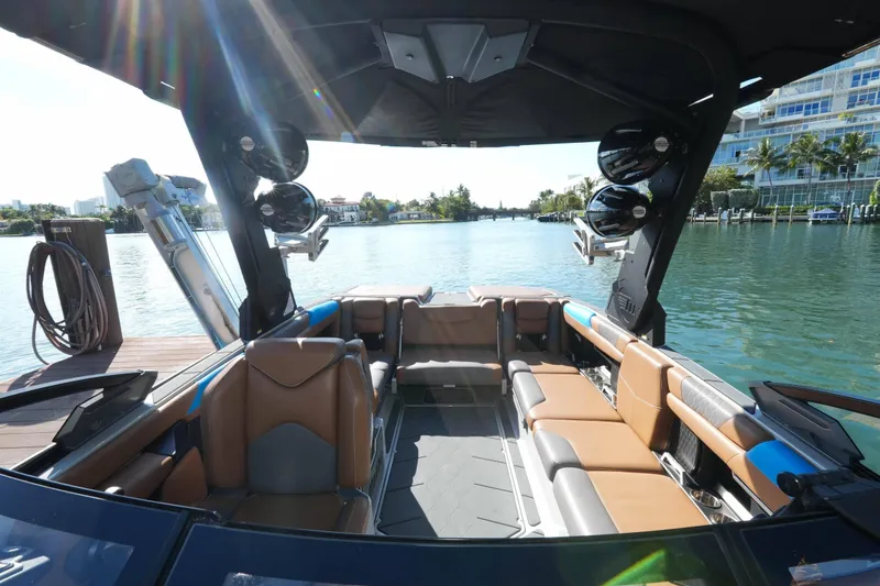 Slide: The Image of 2020 Malibu M240 boat interior with luxurious seating and speakers, docked by a scenic waterfront. - 34