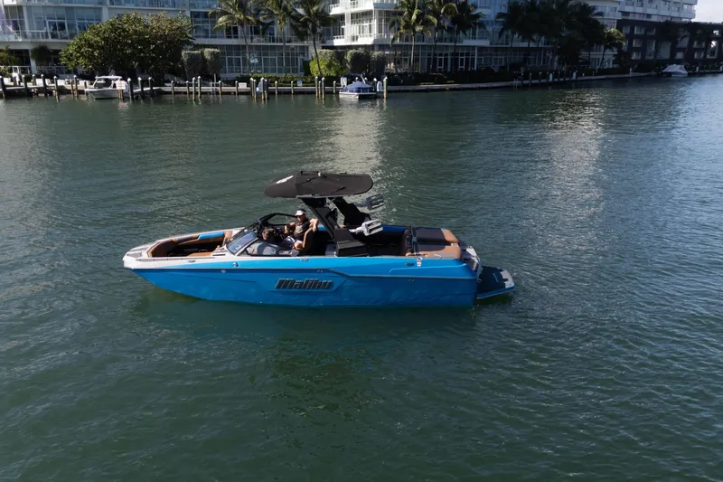 Slide: The Image of 2020 Malibu M240 boat cruising on a calm waterway near waterfront buildings. - 4