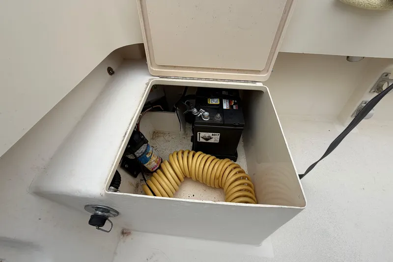 Slide: The Image of Open storage compartment in 2003 Parker 21SE Center Console boat, showing battery and coiled hose. - 22