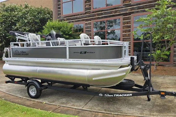 Slide: The Image of 2026 Sun Tracker Bass Buggy 16 XL Select pontoon boat on trailer, parked outdoors. - 6
