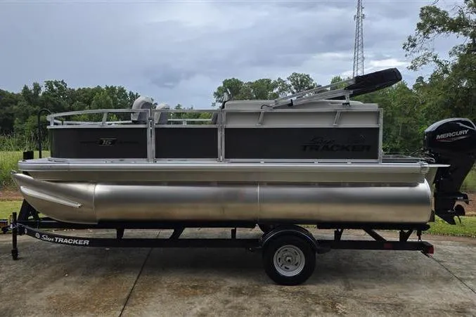 Slide: The Image of 2026 Sun Tracker Bass Buggy 16 XL Select pontoon boat on trailer, parked outdoors. - 2