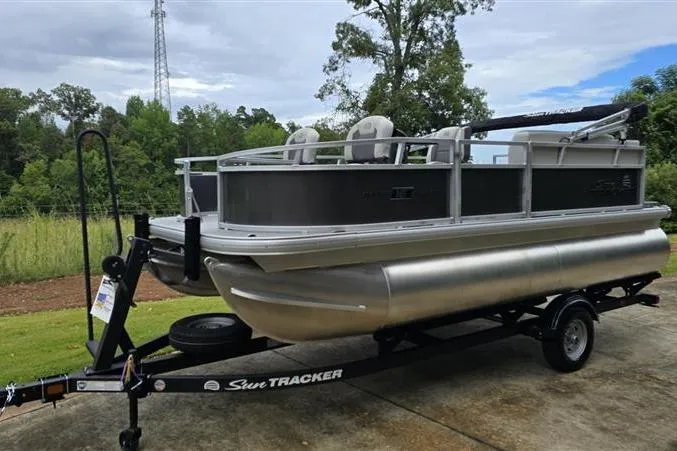 Slide: The Image of 2026 Sun Tracker Bass Buggy 16 XL Select pontoon boat on trailer, parked outdoors. - 1