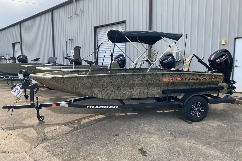 The Image of 2026 Tracker Grizzly 1756 T Marsh boat with Mercury engines, parked outside a warehouse. - 0