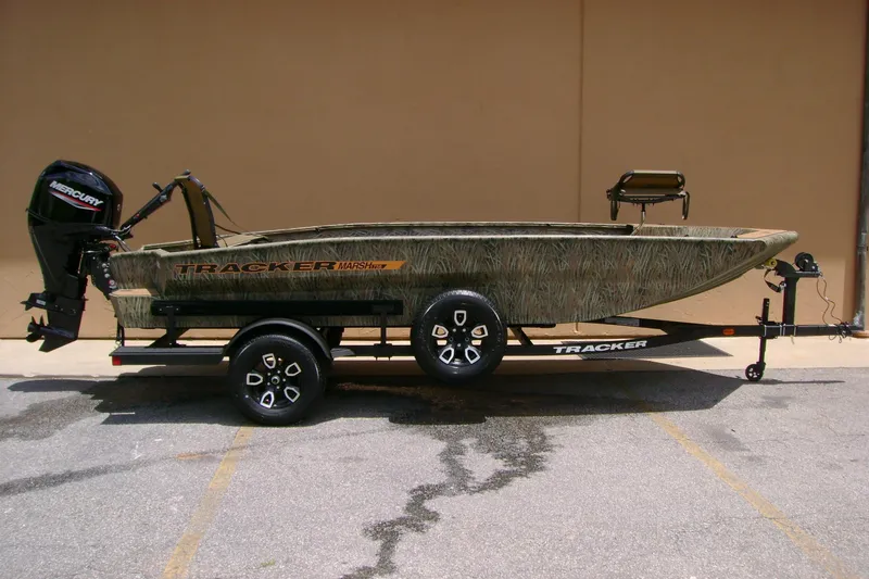 The Image of 2026 Tracker Grizzly 1756 T Marsh boat on trailer, camo design, parked outdoors. - 0