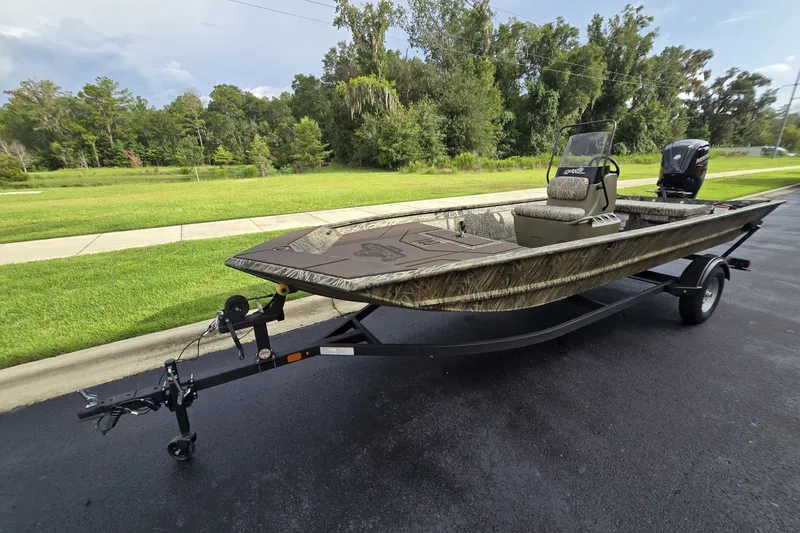 The Image of 2026 Tracker Grizzly 1860 CC boat on trailer, parked on a road near lush greenery. - 0