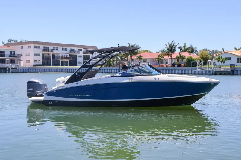 The Image of 2020 Regal LX4 boat cruising on a sunny waterfront with modern buildings. - 0