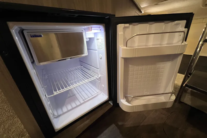 Slide: The Image of Open mini fridge inside 2020 Regal 26 XO boat, featuring shelves and door storage. - 51