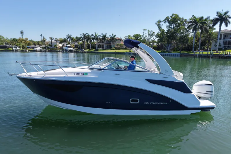 Slide: The Image of 2020 Regal 26 XO boat cruising on a calm lake with palm trees in the background. - 6