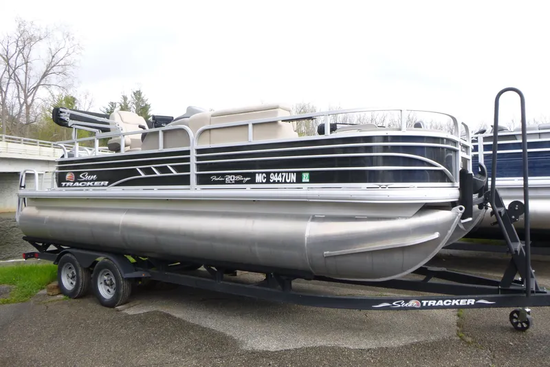 The Image of 2021 Sun Tracker Fishin' Barge 20 DLX pontoon boat on trailer, parked outdoors. - 1
