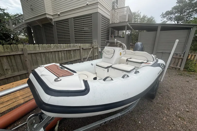 Slide: The Image of 2022 Walker Bay Venture 14 inflatable boat parked on a trailer near a house. - 2