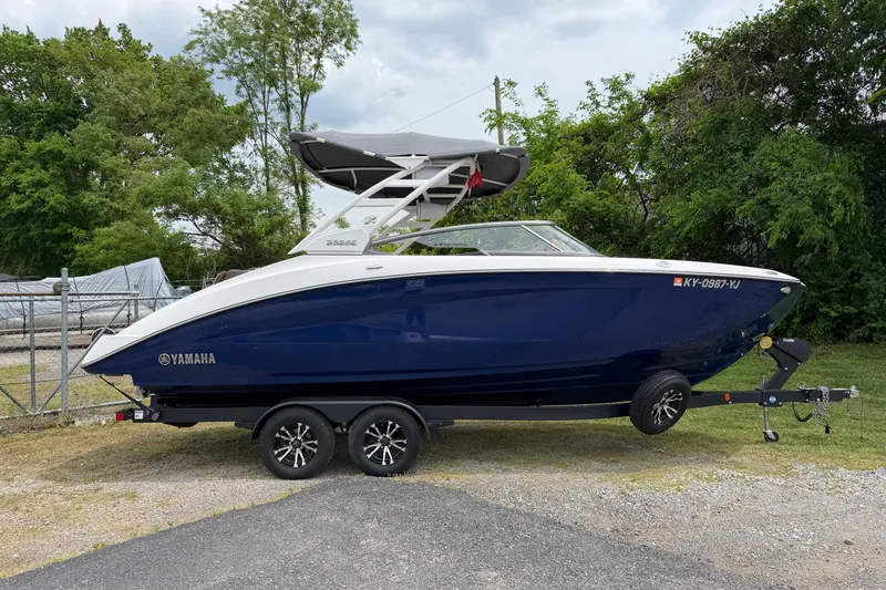 The Image of 2022 Yamaha Boats 252SE on trailer, parked outdoors with lush greenery background. - 0