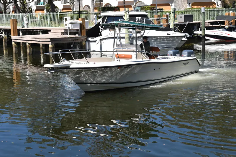Slide: The Image of 2001 Pursuit 2470 Center Console boat navigating a marina with docked vessels. - 2