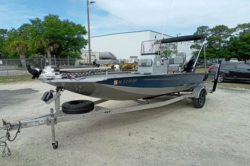 Slide: The Image of 2021 Xpress H20B Bay boat on trailer, parked outdoors with trees and buildings in background. - 5