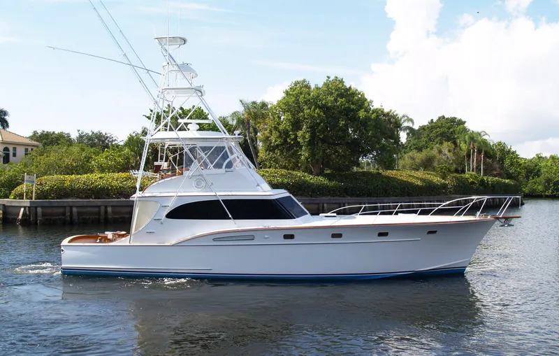 The Image of 1983 Rybovich 55 Convertible yacht cruising on a calm river with lush greenery. - 0