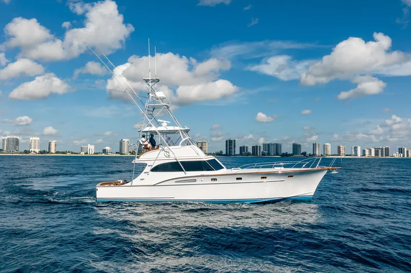 Slide: The Image of 1983 Rybovich 55 Convertible yacht cruising on ocean with city skyline backdrop. - 114