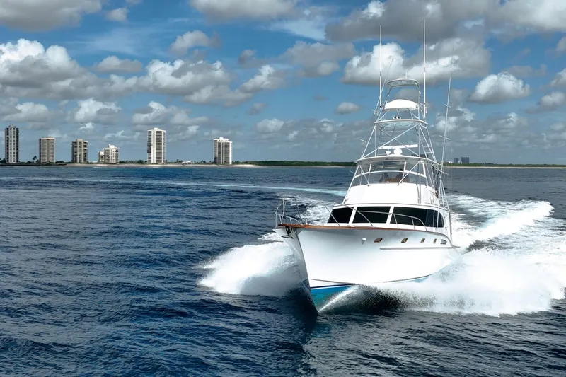 Slide: The Image of 1983 Rybovich 55 Convertible yacht cruising on open water with city skyline backdrop. - 126