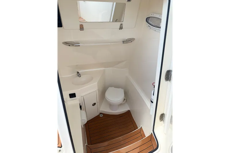 Slide: The Image of 2016 Cobia 277 Center Console boat interior with compact bathroom and wooden flooring. - 16