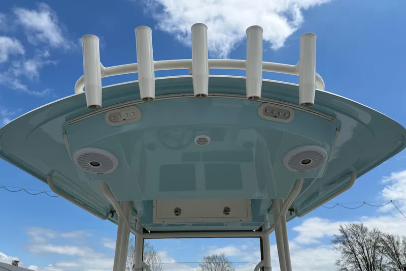 Slide: The Image of 2016 Cobia 277 Center Console boat top with rod holders and speakers under blue sky. - 25