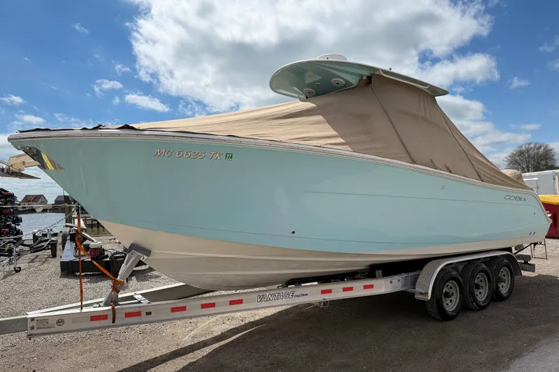 Slide: The Image of 2016 Cobia 277 Center Console boat on trailer, covered, under a partly cloudy sky. - 48