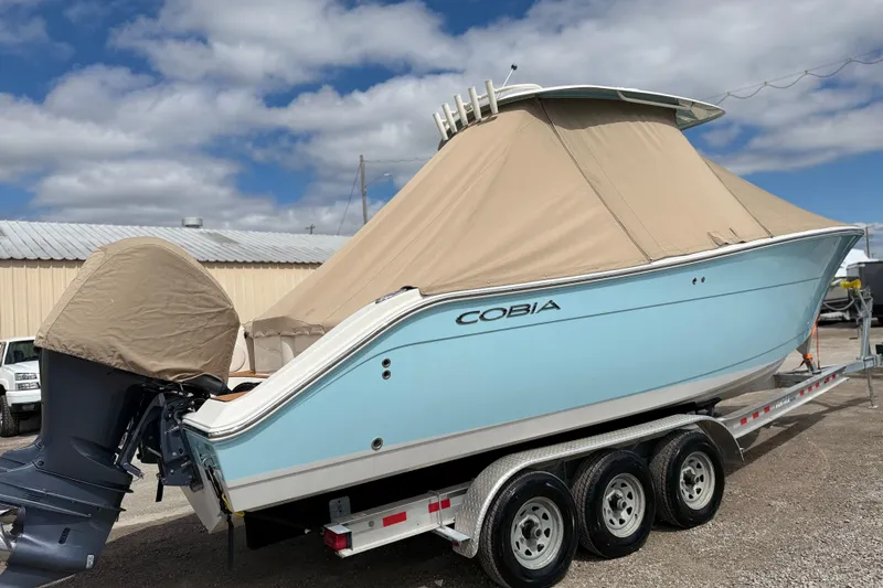 Slide: The Image of 2016 Cobia 277 Center Console boat on trailer, covered, under a partly cloudy sky. - 49