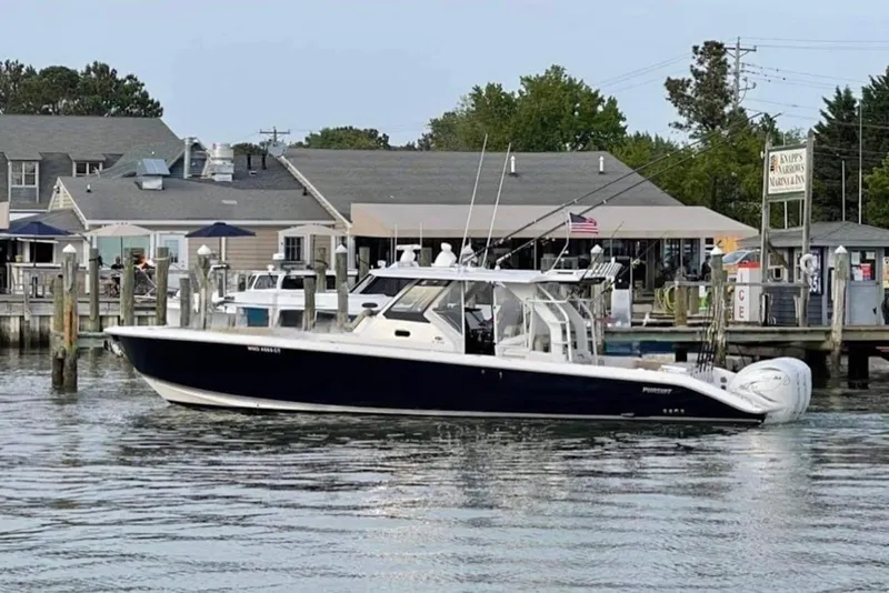 The Image of 2019 Pursuit S 408 Sport boat docked at a marina with waterfront buildings. - 0