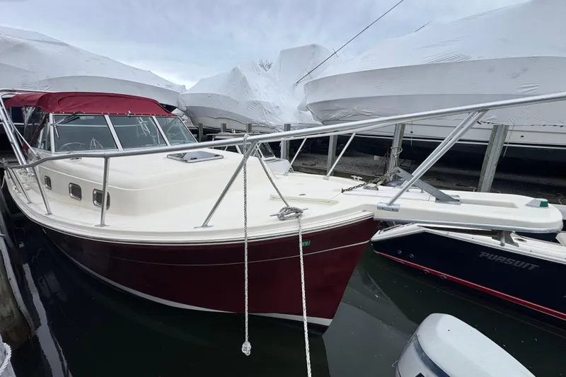 Slide: The Image of 2001 Mainship Pilot 30 boat docked, featuring a maroon hull and covered deck. - 2