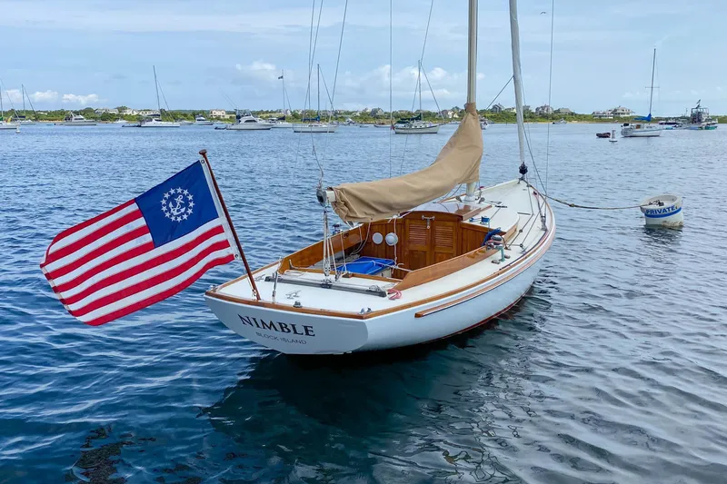 Slide: The Image of 2003 Herreshoff Alerion 26 sailboat named Nimble on calm water, displaying a historical American flag. - 1