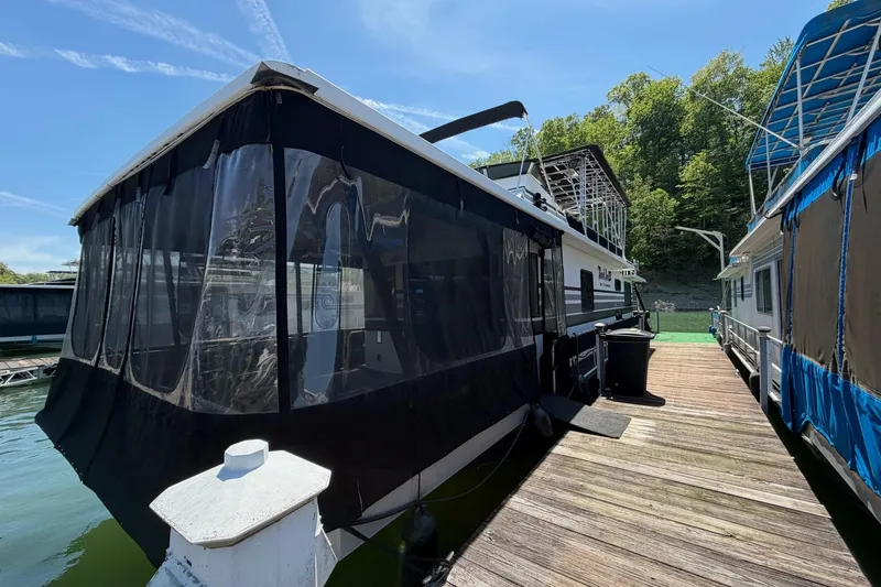 Slide: The Image of 1989 Sumerset 14x62 houseboat docked, featuring black canvas enclosure and wooden walkway. - 38