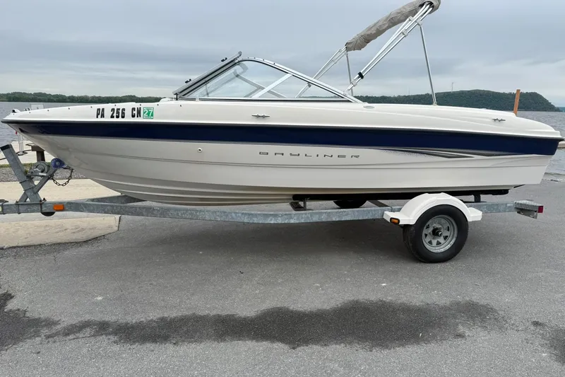 The Image of 2003 Bayliner 185 boat on trailer, parked near a lake with overcast skies. - 1