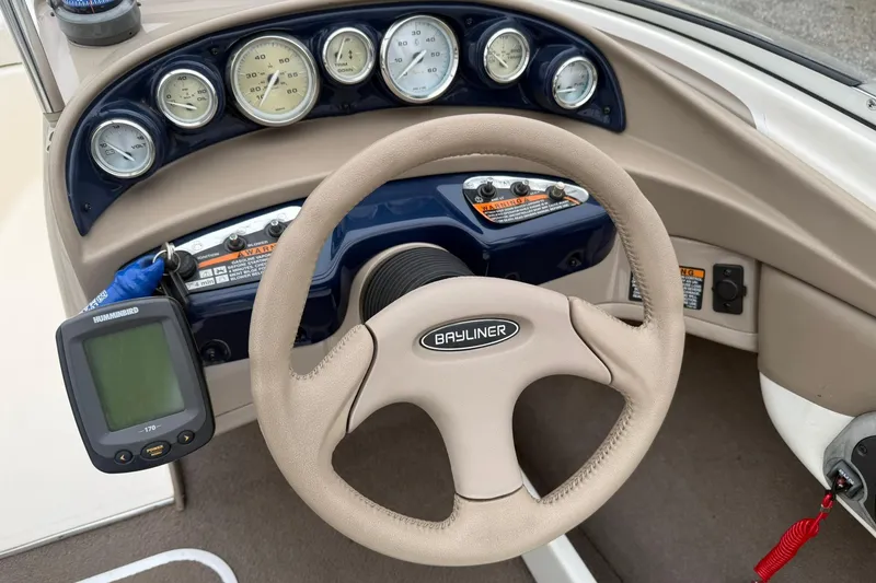 Slide: The Image of Steering wheel and dashboard of a 2003 Bayliner 185 boat with gauges and controls. - 14