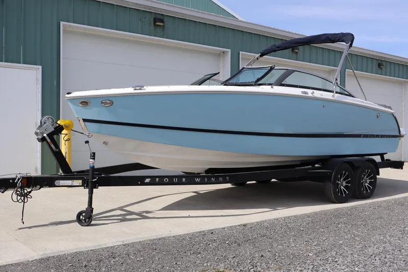 The Image of 2026 Four Winns H4 boat on trailer, parked outside a green building. - 0