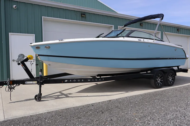 Slide: The Image of 2026 Four Winns H4 boat on trailer, parked outside a green building. - 2