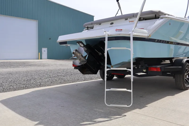 Slide: The Image of 2026 Four Winns H4 boat on trailer with ladder, parked near a large building. - 6