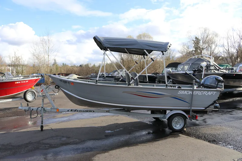The Image of 2016 Smoker Craft Alaskan 15 boat on trailer, parked outdoors under cloudy sky. - 1